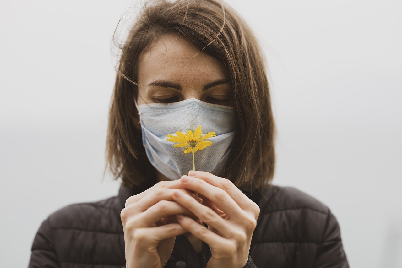 mujer de frente con cubrebocas y flor en sus manos por coronavirus